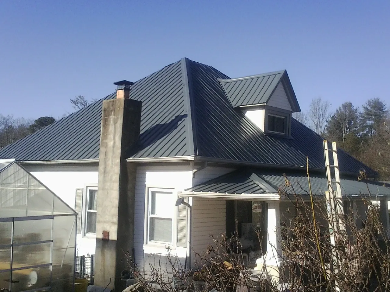 Dark blue standing seam metal roof on a white farmhouse with dormer — Slate & Tile Roof Repair by Roofing Brothers in Blissfield