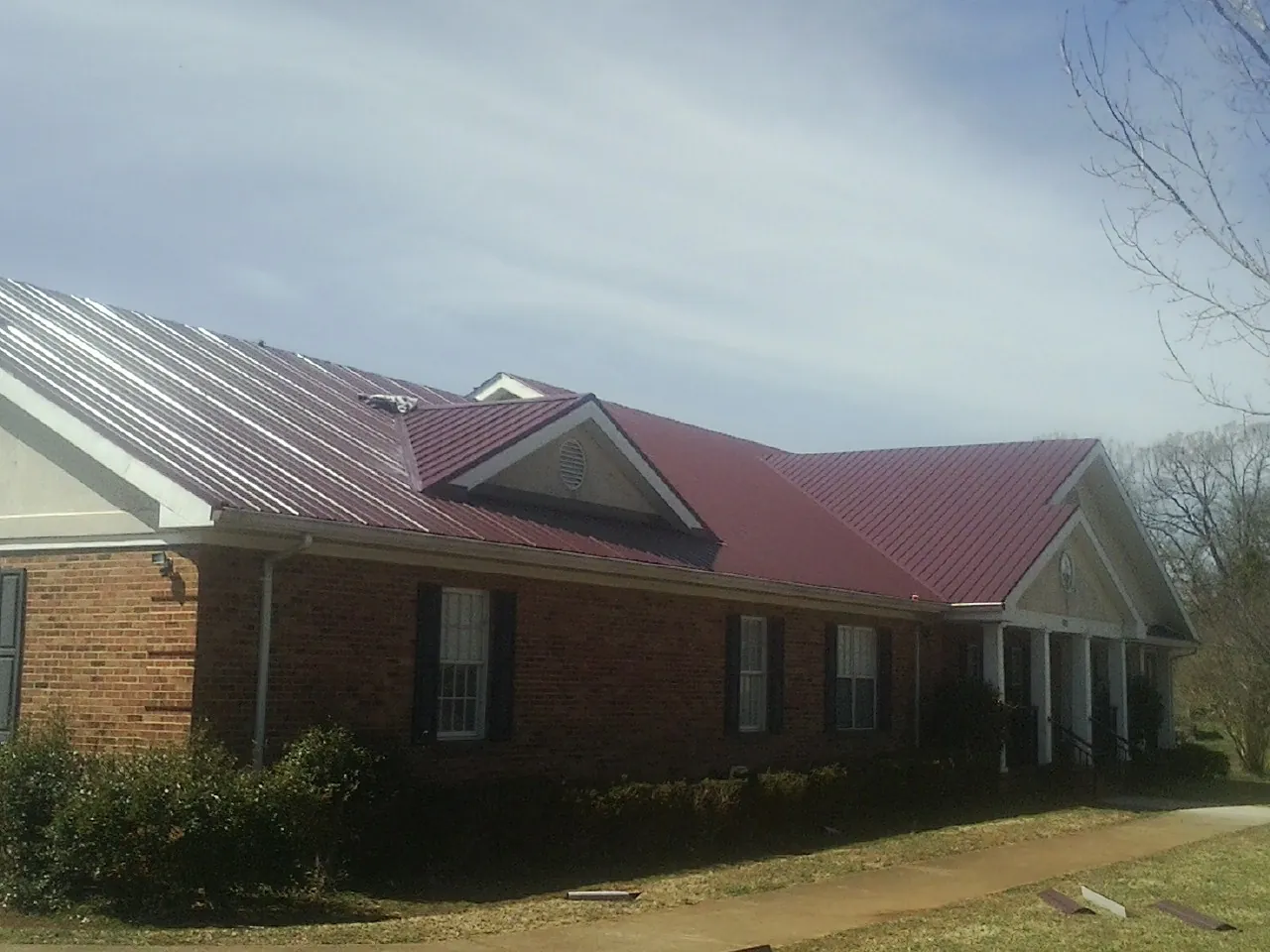 Red metal roof with gabled entries on a long brick building, from a Hail Damage Roof Repair job in Blissfield