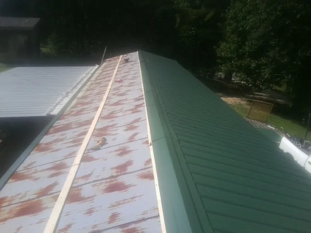 Old rusted panels beside newly installed green metal roofing — Wind Damage Roof Repair by Roofing Brothers in Blissfield