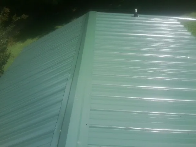 New green metal panels meeting at the ridge of a roof — Flat Roof Repair work by our crew in Blissfield