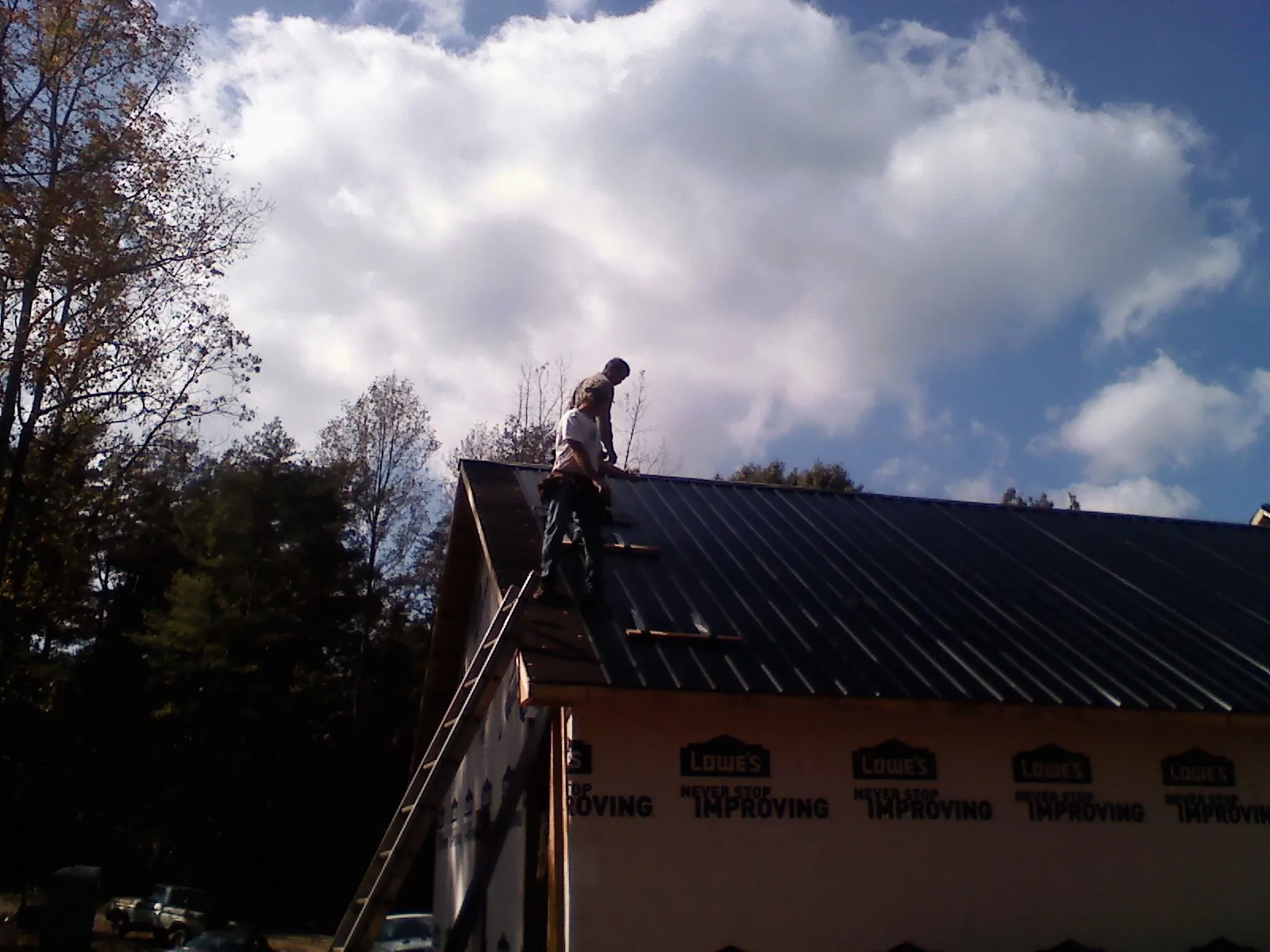Roofer fastening dark metal panels high against a cloudy sky, from a Roof Inspection job in Blissfield