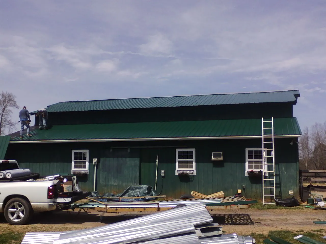 Crew installing green metal roofing on a large green barn in Blissfield