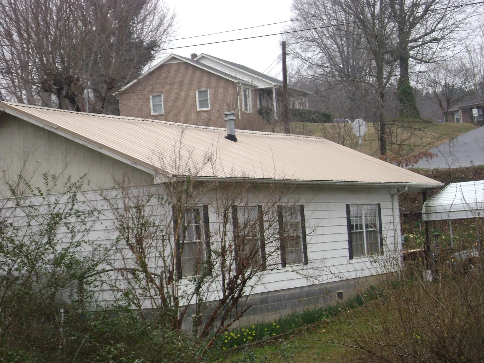 Tan metal roof on a white sided house set into a hillside — Commercial Roofing by Roofing Brothers in Blissfield